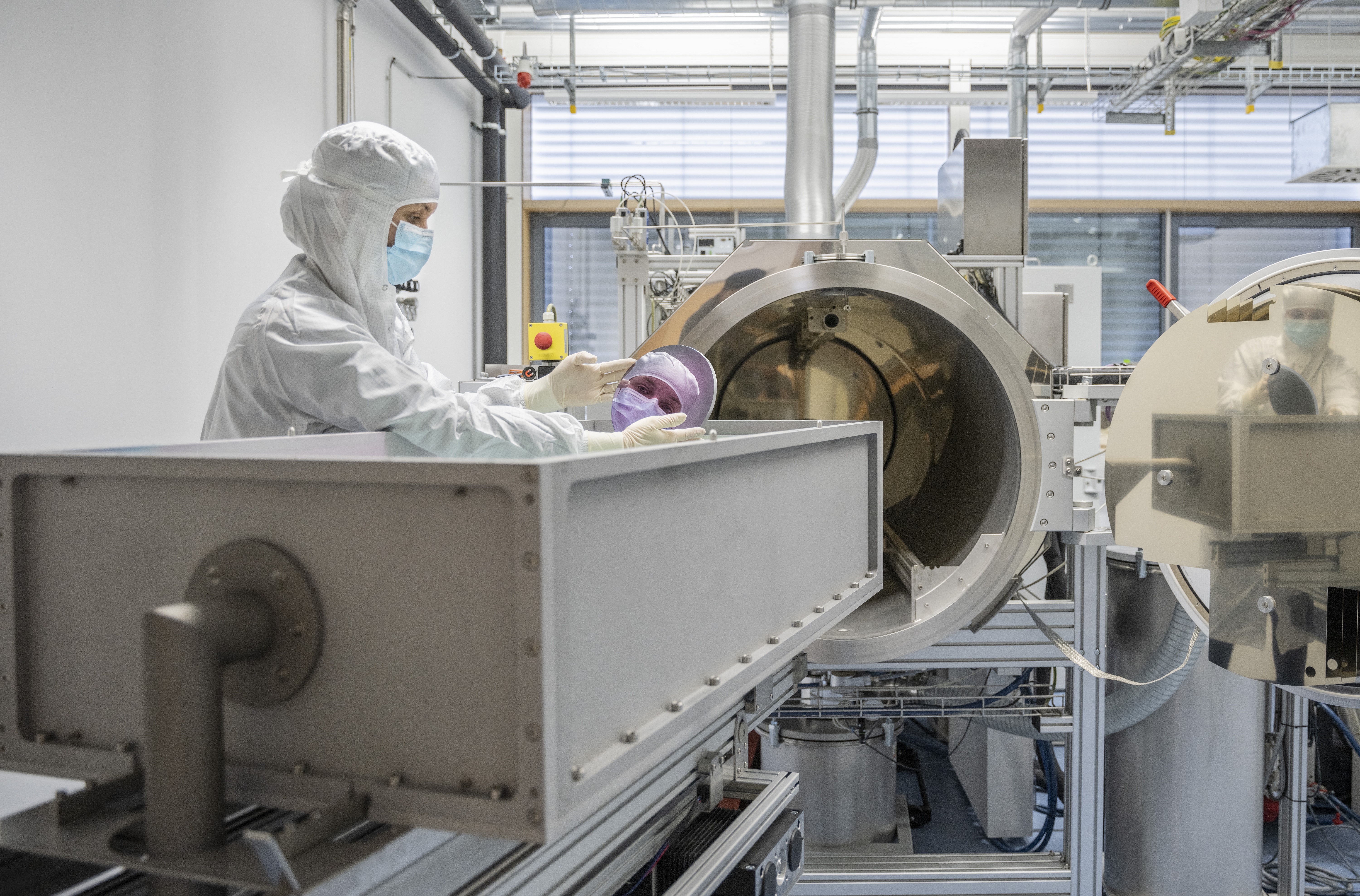 Eine Forscherin mit Labor-Schutzausrüstung  hält einen hochreflektierenden Spiegel für Laseranwendungen in der Hand. 