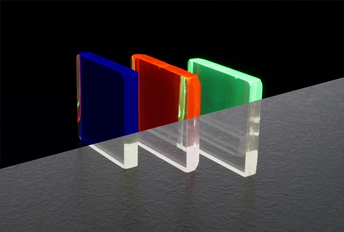 Lumineszierende Gläser leuchten unter ultraviolettem (UV) Licht (oberer Bildteil) und sind unter Raumlicht transparent (unterer Bildteil). Der Farbeindruck wird durch den verwendeten Dotierstoff bestimmt: blau (Thulium), rot (Europium) und grün (Terbium). 